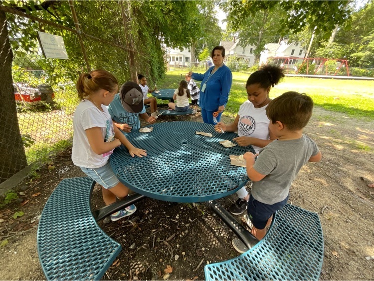 students and a teacher outside exploring fossils at tables under the trees